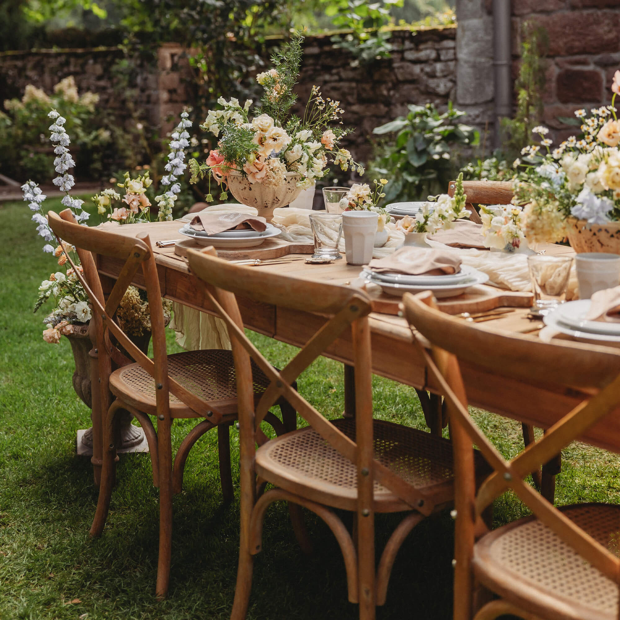 Houten tuintafel met gevlochten stoelen en bloemstukken op groen gras