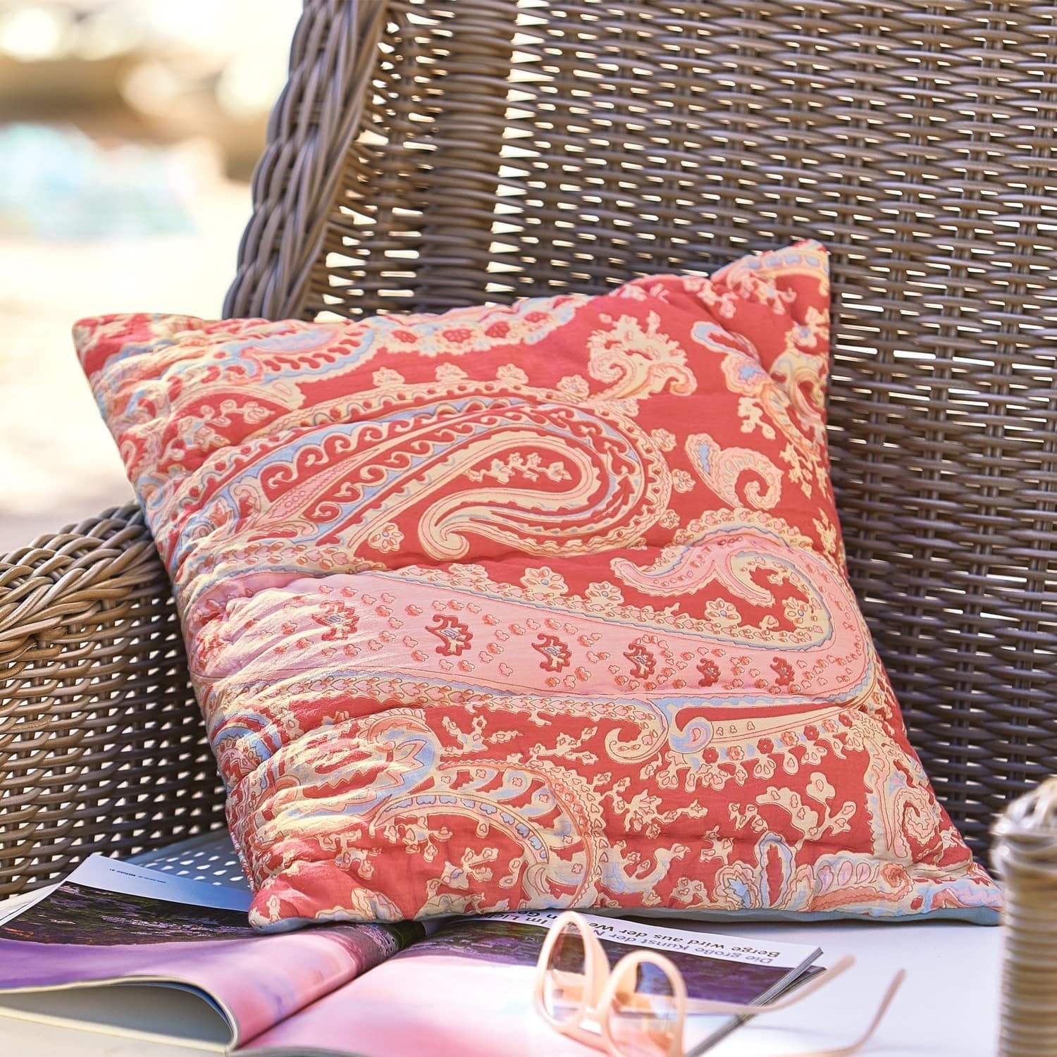 Decoratief katoenen kussen in rood met paisley patroon op een rotan stoel buiten