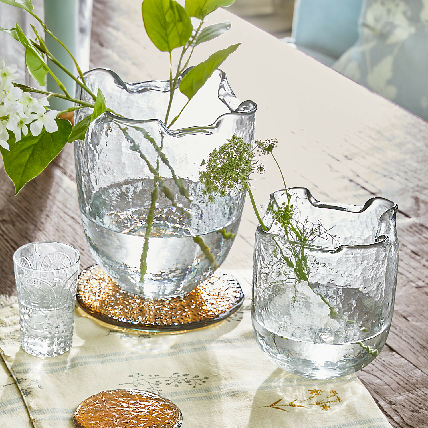 Transparante glazen vazen met golvende rand op houten tafel met groene planten en decoratie