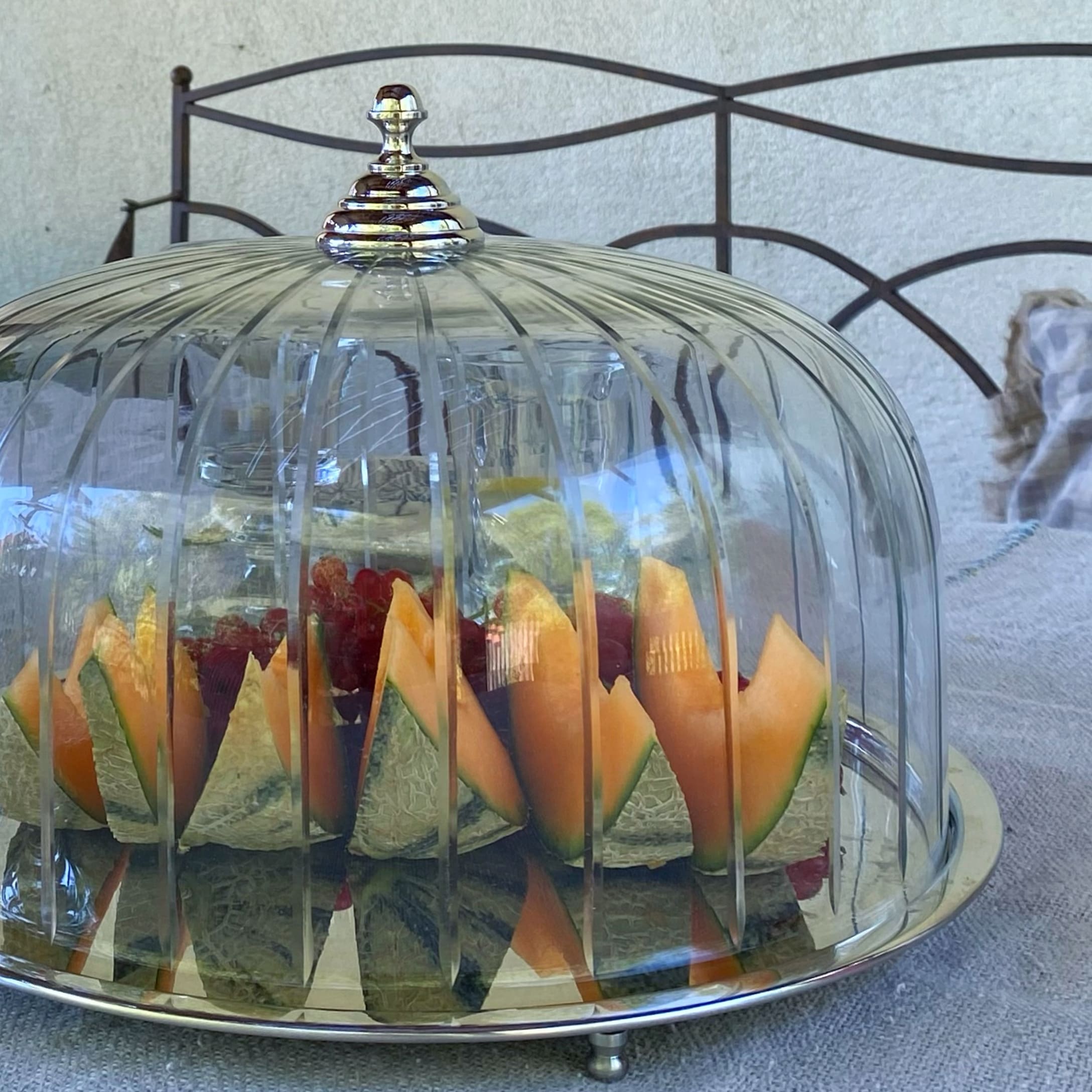 Glazen stolp op metalen schaal met gesneden meloen en fruit op tafel