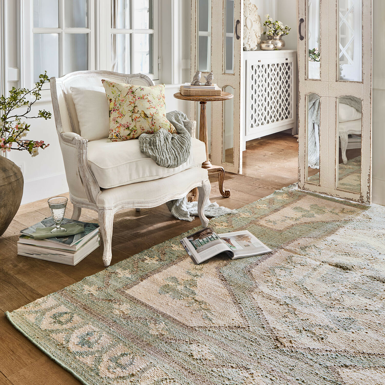 Witte houten fauteuil met bloemenkussen in lichte woonkamer met decoratief vloerkleed