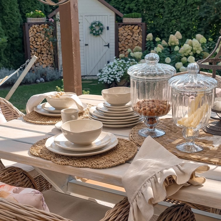 Witte keramiekset op lichte houten tafel met decoratieve glazen potten in de tuin