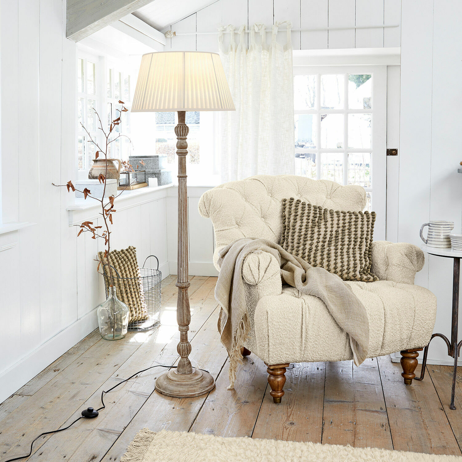 Staande lamp Morten Beige boucle-stoffen fauteuil met kussen en staande lamp in lichte houten woonkamer
