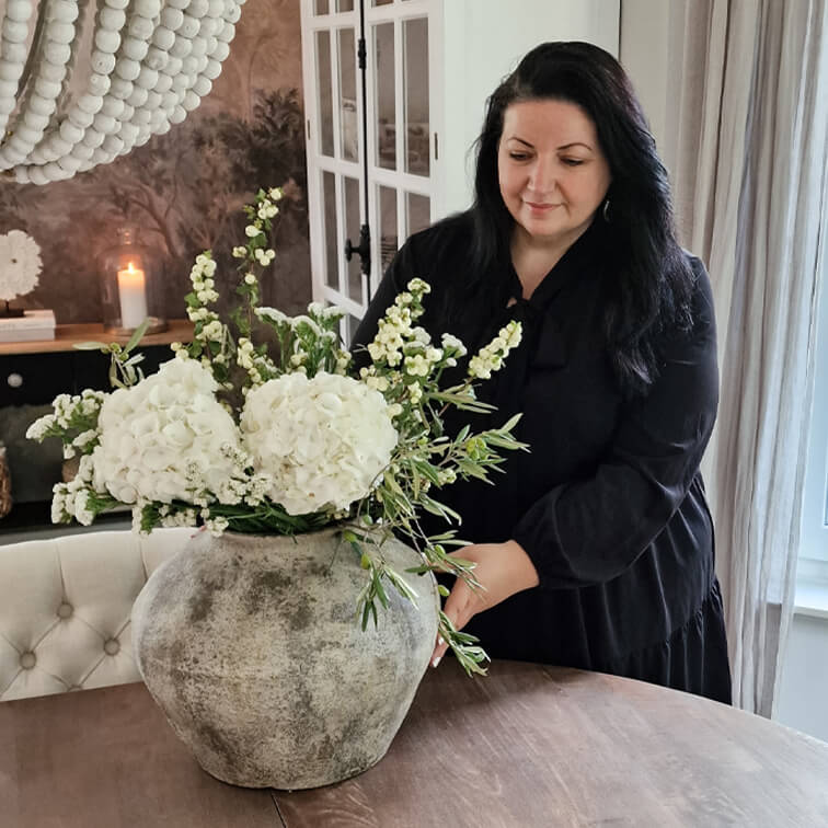 Grote grijze keramische vaas met witte bloemen op houten tafel in een gezellige kamer.