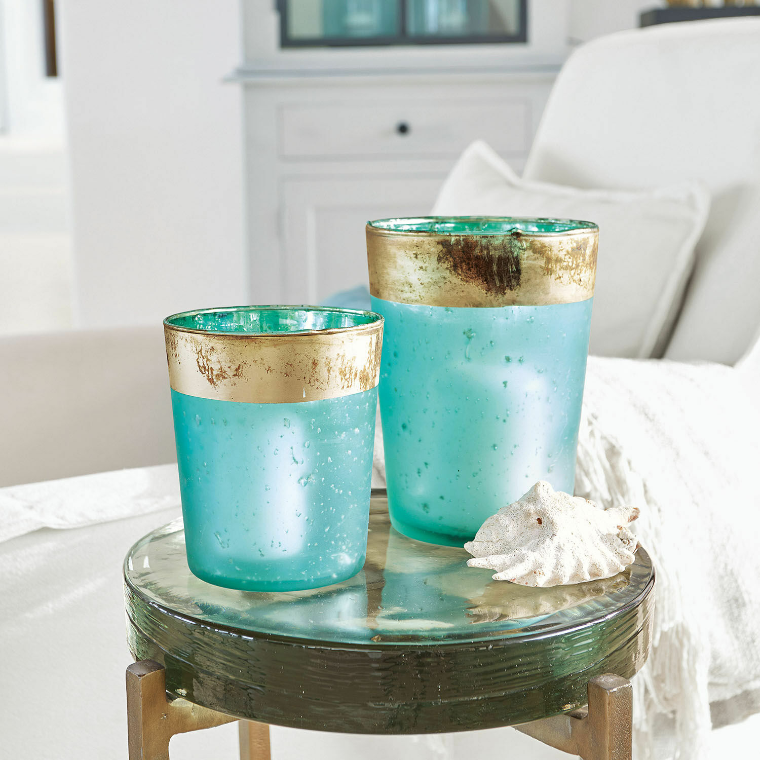 Windlicht set van 2 Ewena Twee turquoise glazen windlichten met gouden rand op een decoratieve glazen tafel