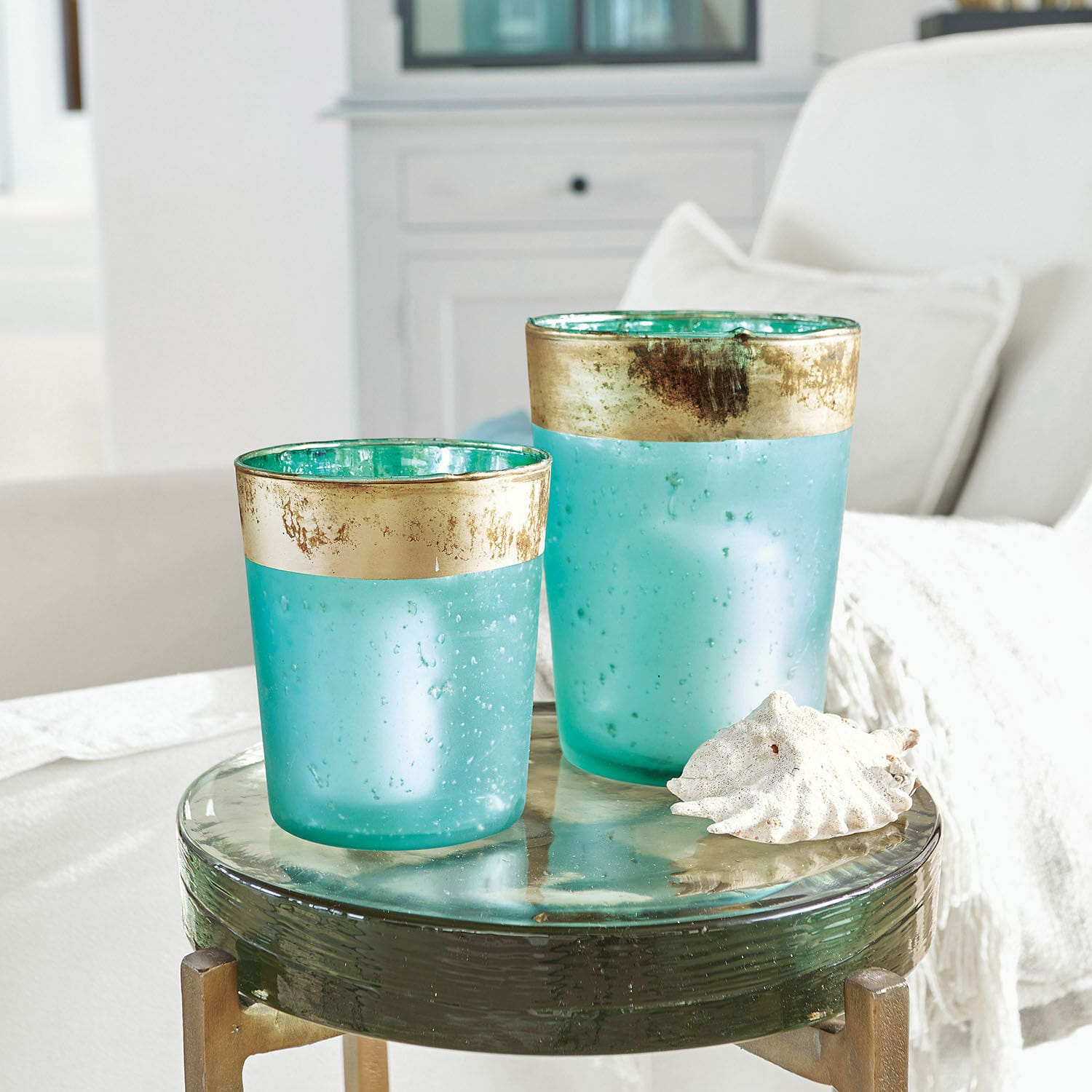 Windlicht set van 2 Ewena Twee turquoise glazen windlichten met gouden rand op een decoratieve glazen tafel