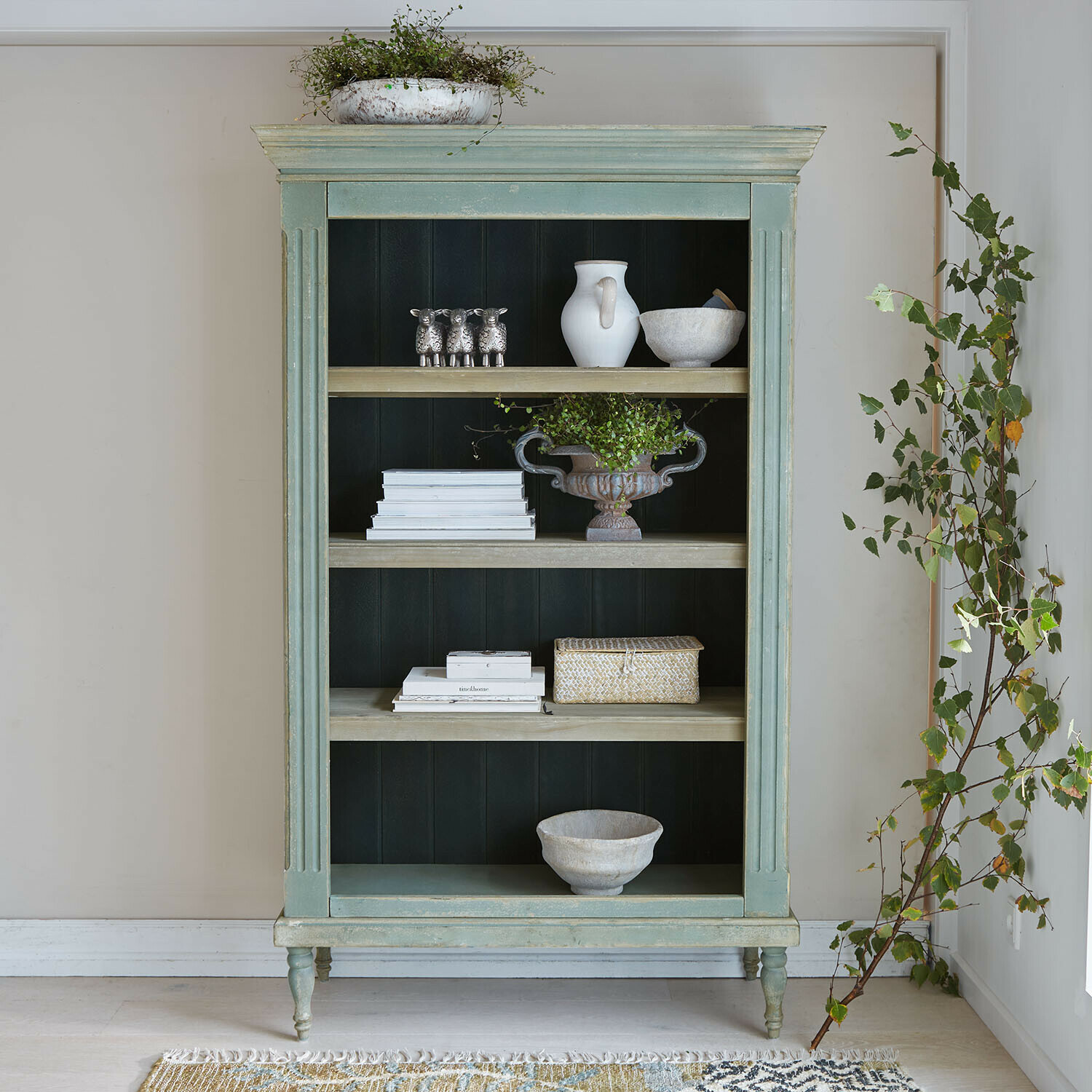 Groene houten kast met planken, gedecoreerd met planten en wit servies, vintage stijl