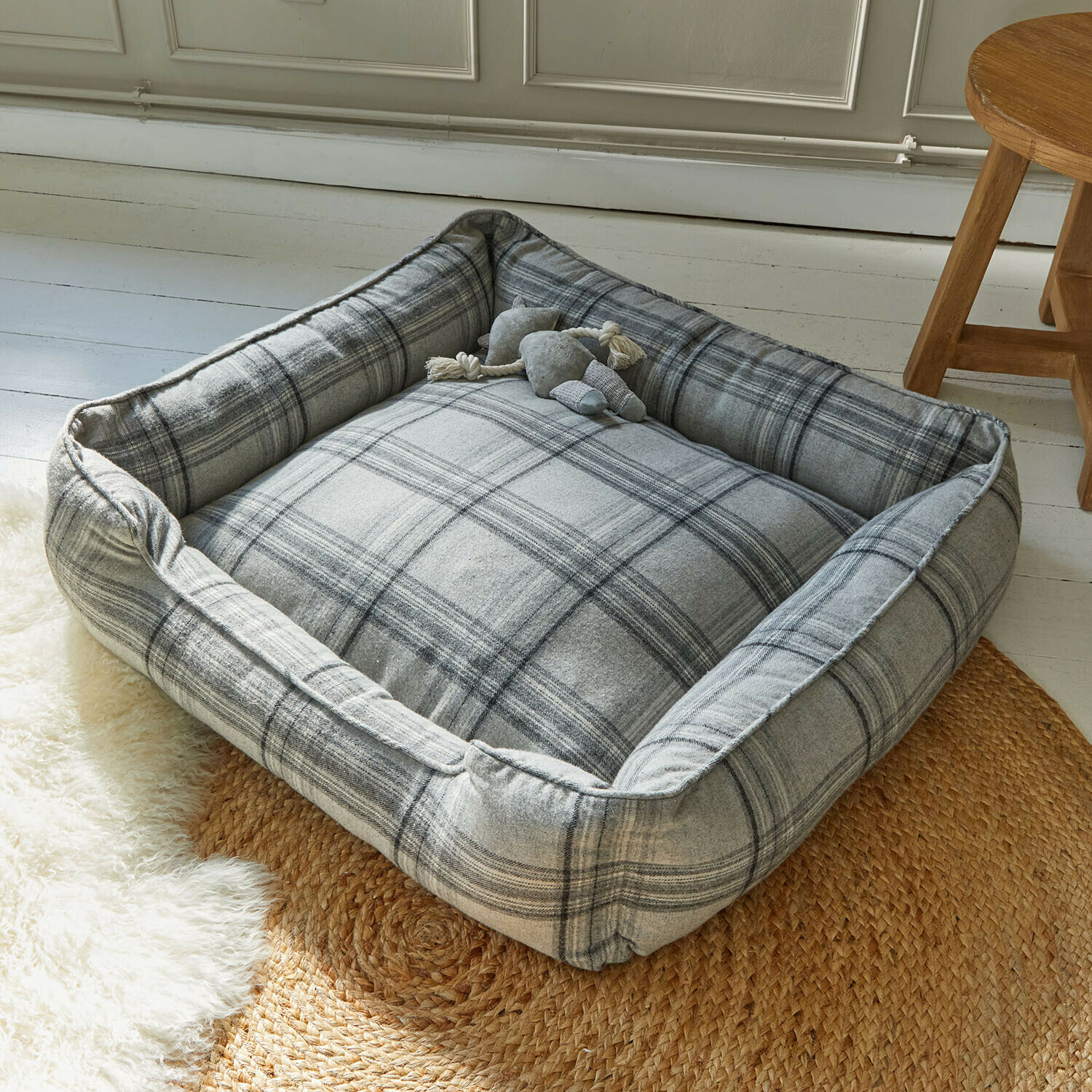 Grijs geruit hondenbed van zacht materiaal op gevlochten vloerkleed in lichte kamer