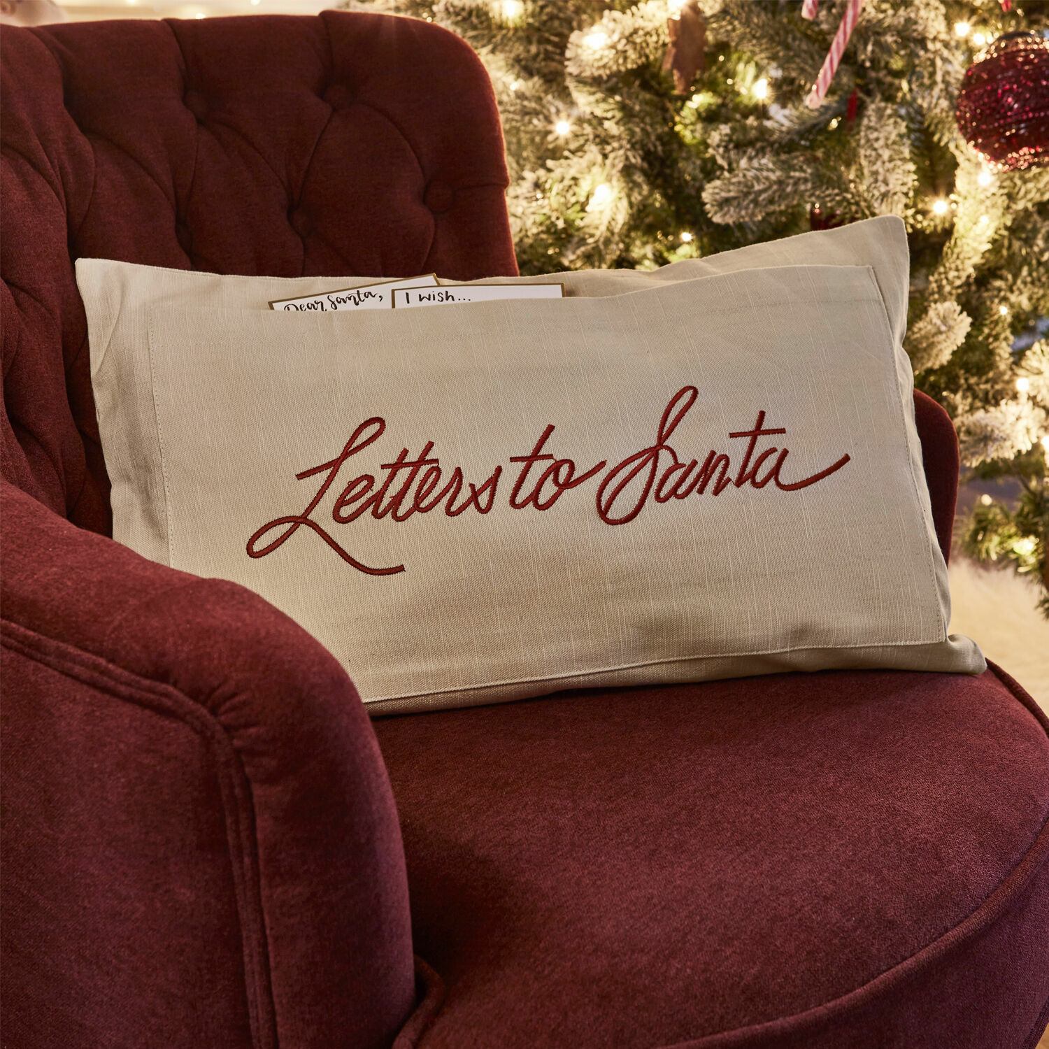 Kussenhoes Welenzas Beige linnen kussen met rode tekst Letters to Santa op bordeauxrode stoel bij kerstboom