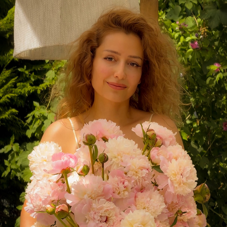Vrouw met lang haar houdt een grote bos roze pioenrozen vast tegen een groene tuinachtergrond