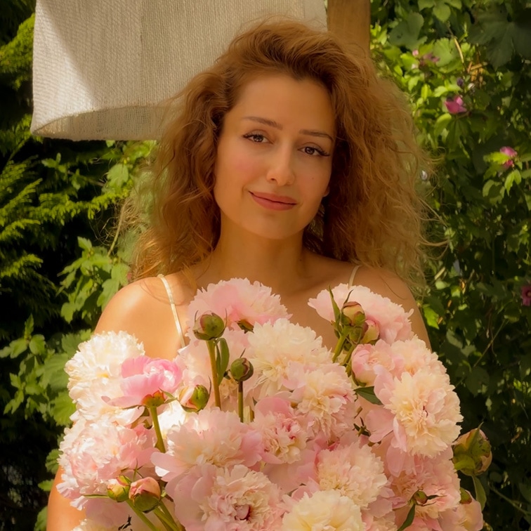 Vrouw met lang haar houdt een grote bos roze pioenrozen vast tegen een groene tuinachtergrond