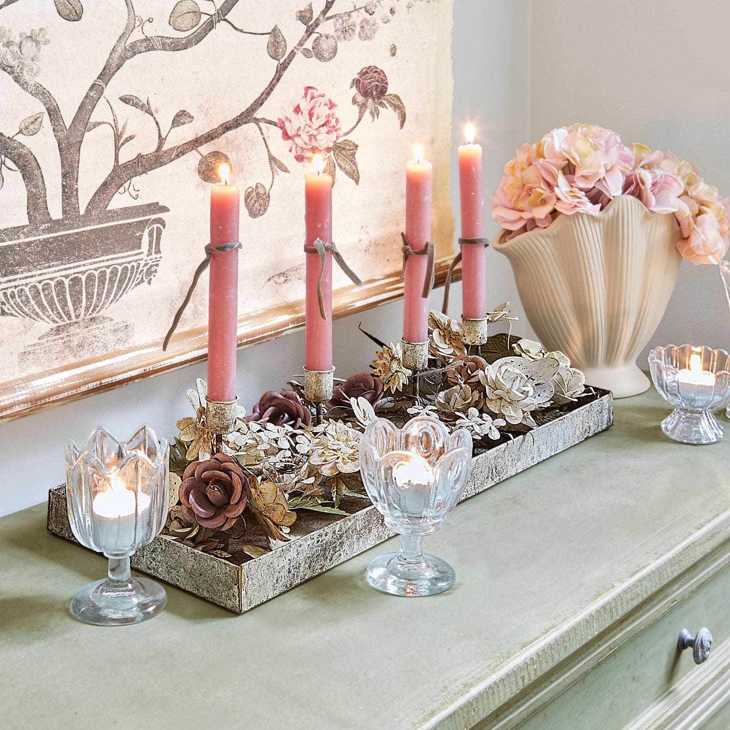 Decoratieve kandelaar met metalen bloemen en roze kaarsen op groene tafel met vaas