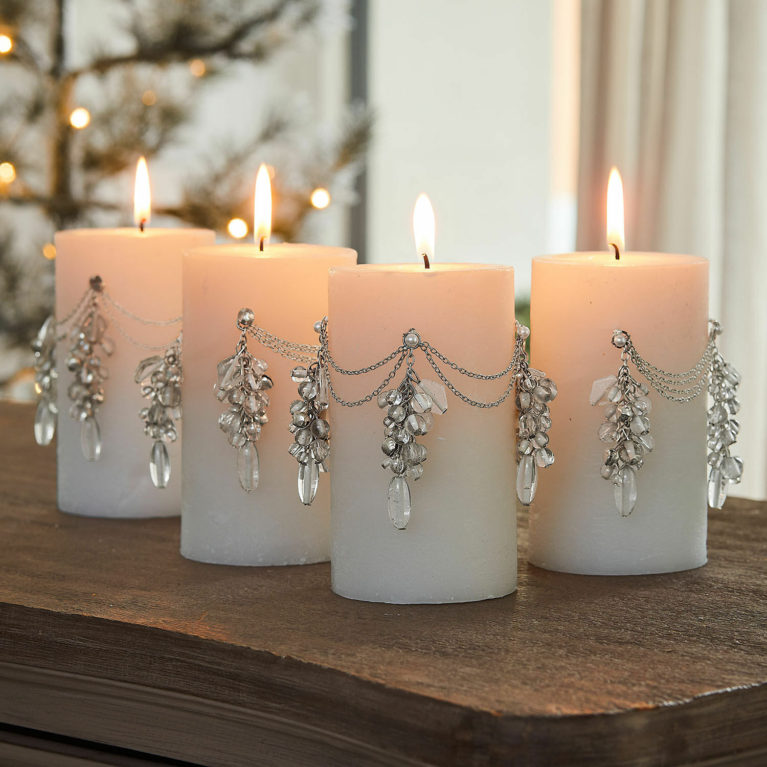 Sierpin set van 4 Gisolée Set van vier witte kaarsen versierd met zilveren kettingen en kristallen hangers op een houten tafel