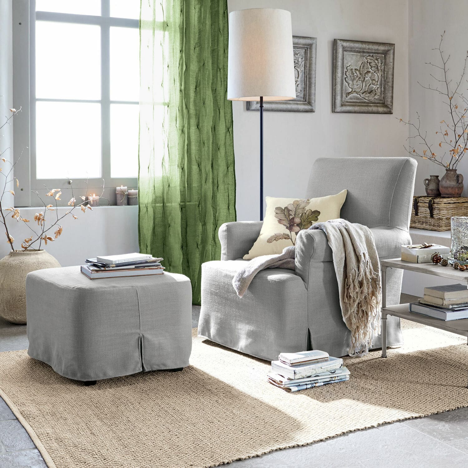 Fauteuil met hocker Nasour Grijze gestoffeerde fauteuil met voetenbank en groene gordijnen in lichte woonkamer met jute vloerkleed