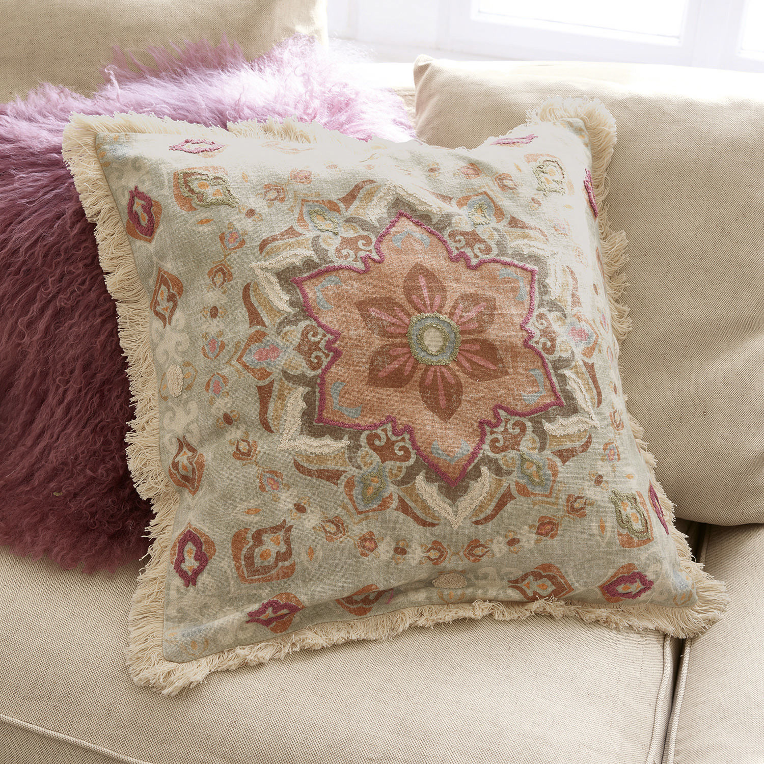 Decoratief katoenen kussen met franjes en pastelkleurig patroon op beige bank