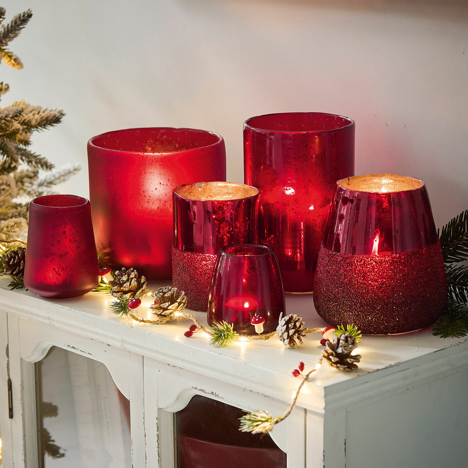 Windlicht set van 6 Paro Set rode glazen windlichten in verschillende vormen op een witte kast met kerstdecoratie