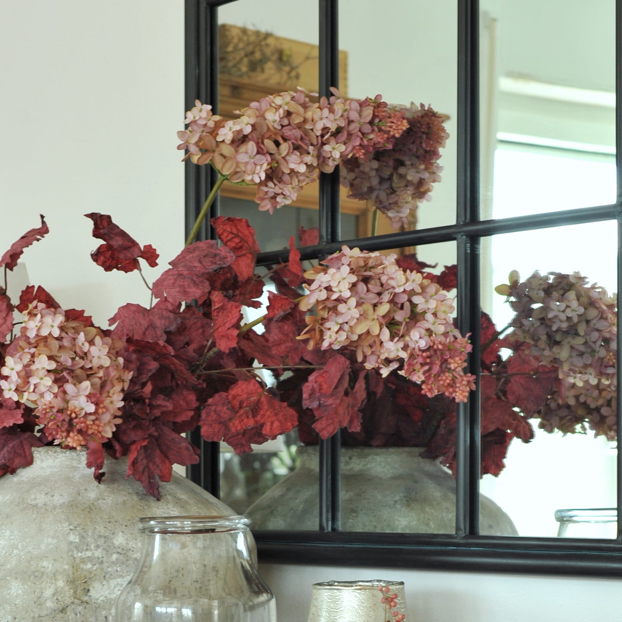 Decoratieve stenen vaas met rode bladeren en roze bloemen voor een zwarte spiegel