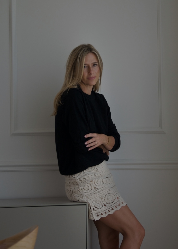 Vrouw in zwarte trui en crèmekleurige kanten rok zittend op kast in minimalistisch interieur