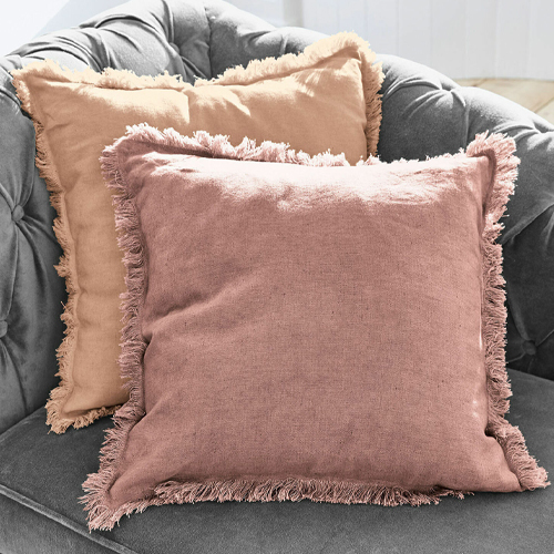 Twee decoratieve linnen kussens in roze en beige met franjes op een grijze bank, gezellige sfeer
