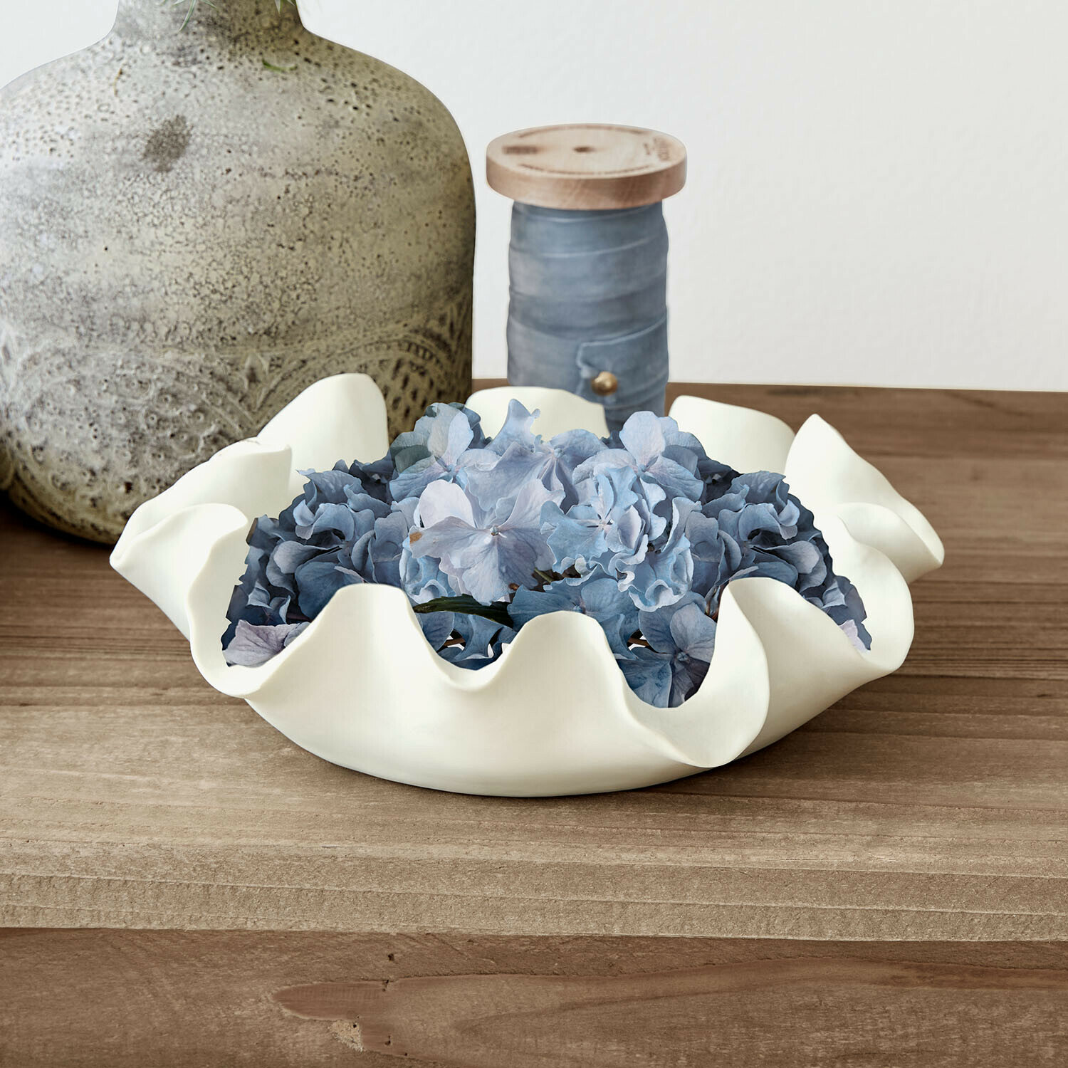 Witte keramische schaal met golvende rand en blauwe bloemen op houten tafel