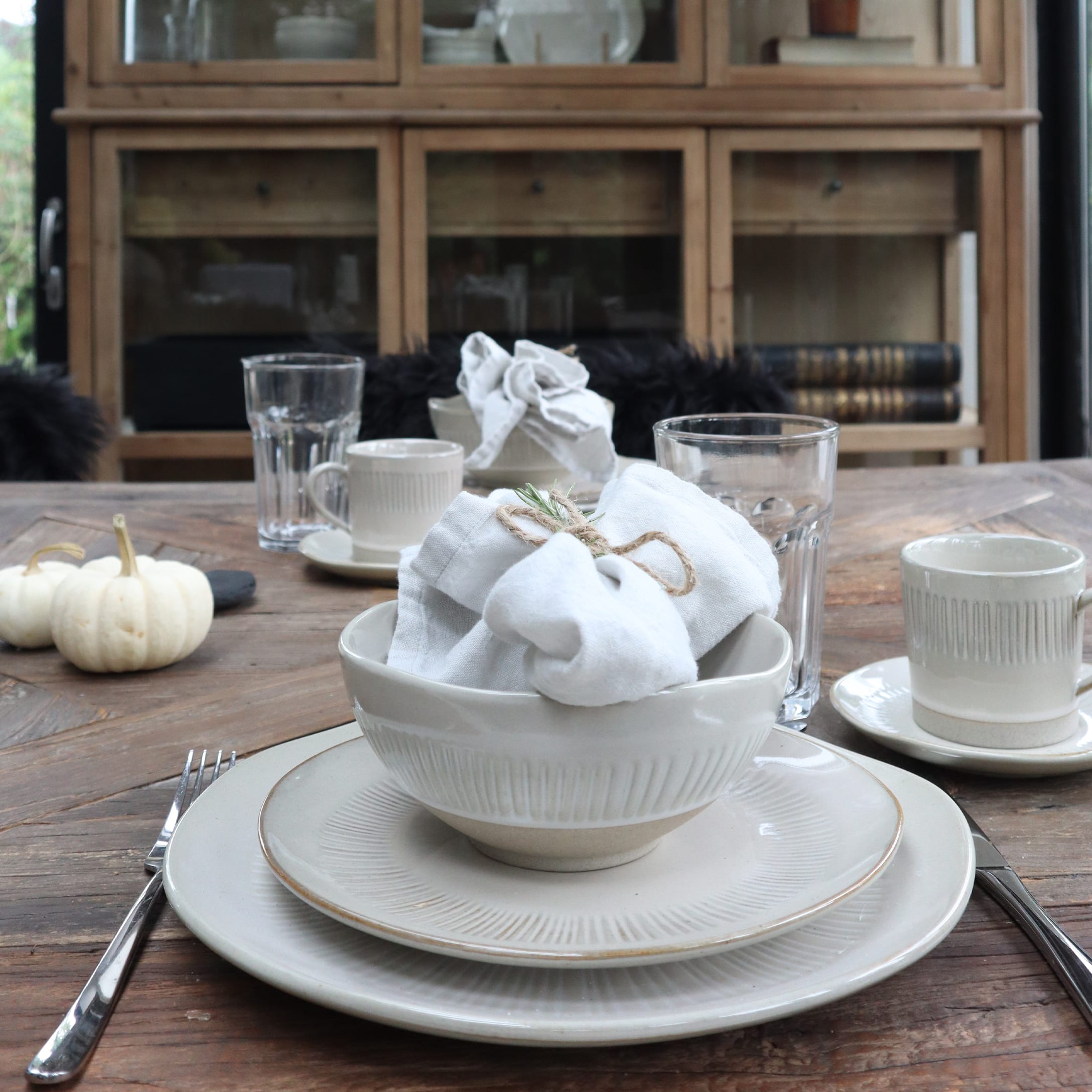 Set crème keramiek op houten tafel met witte servetten en glazen in rustieke stijl