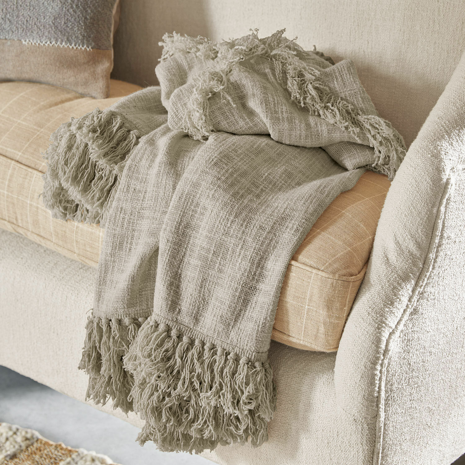 Plaid Freya Beige plaid met franjes van zacht materiaal op lichte bank, sfeervolle woondecoratie