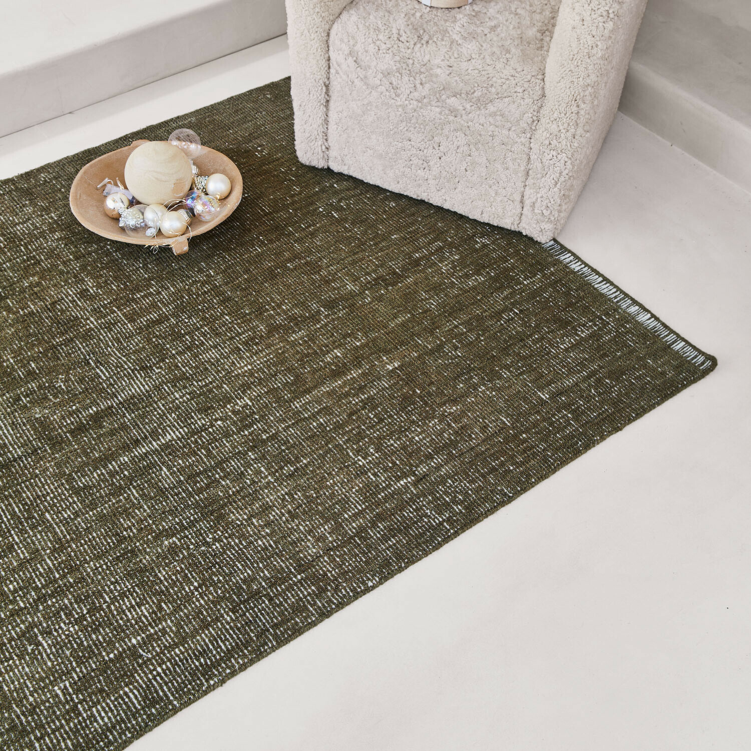 Groen vloerkleed met subtiel patroon naast een crèmekleurige stoel en decoratie op de vloer