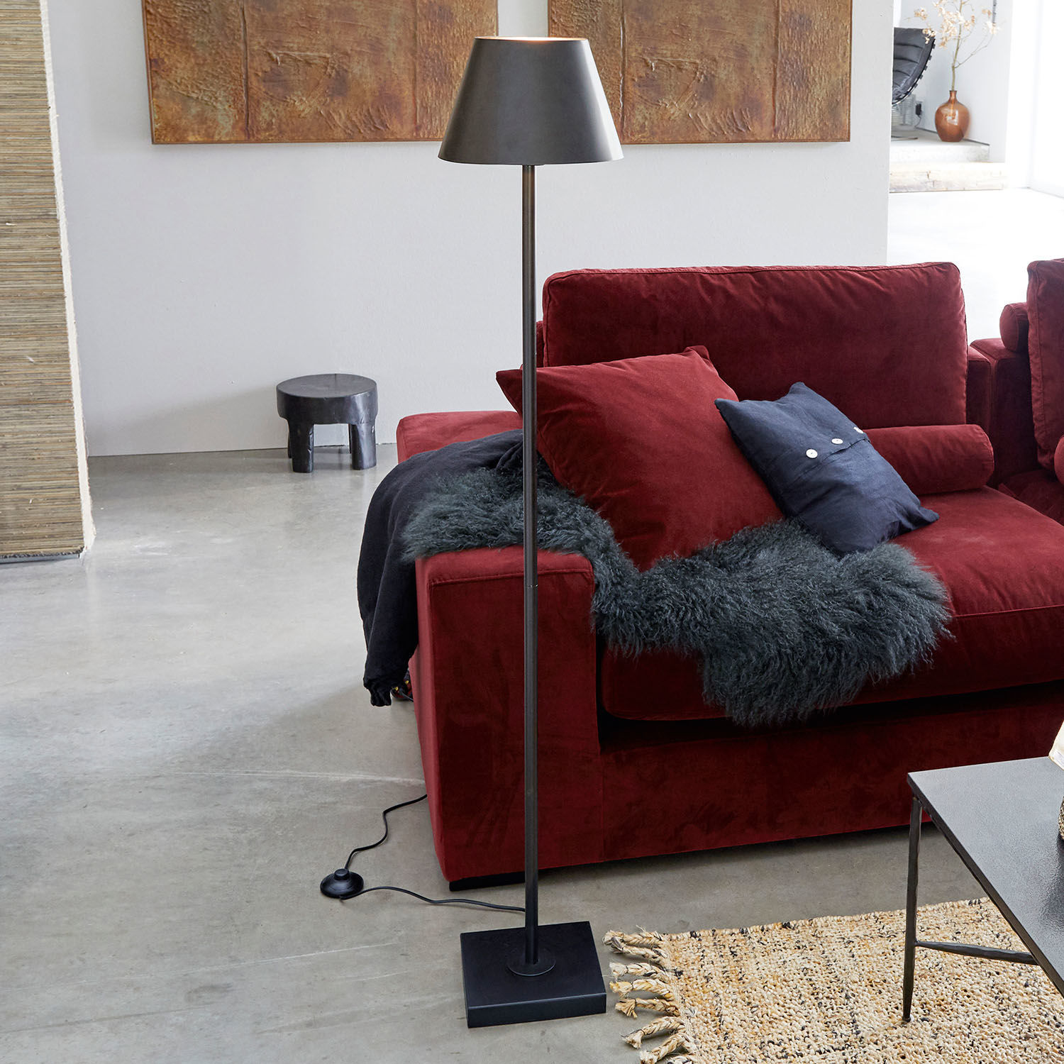 Staande lamp Marjan Zwarte metalen vloerlamp met kap naast rode bank en vloerkleed in moderne woonkamer