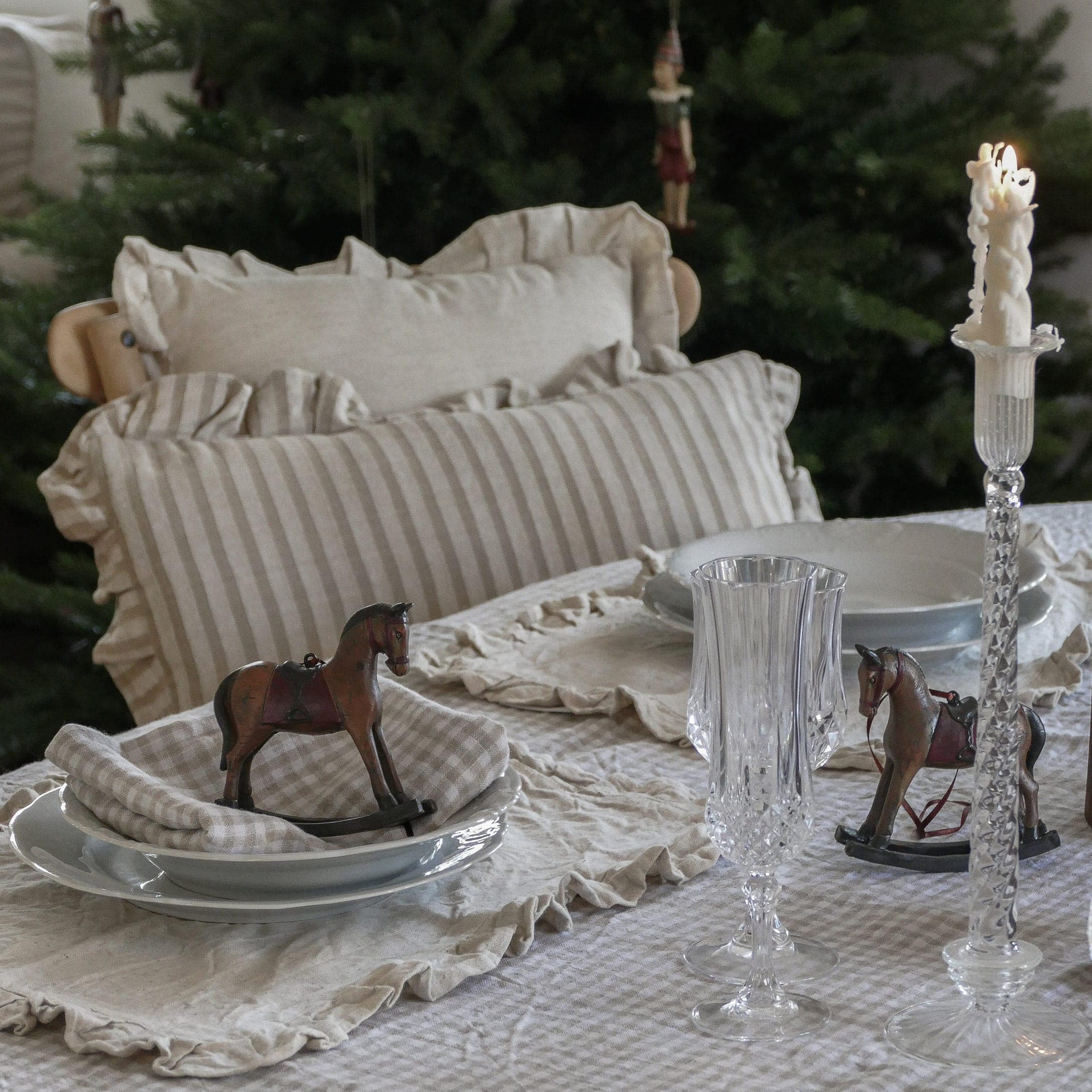 Rustieke tafel met beige linnen tafelkleed en gestreepte kussens plus houten hobbelpaard decoratie