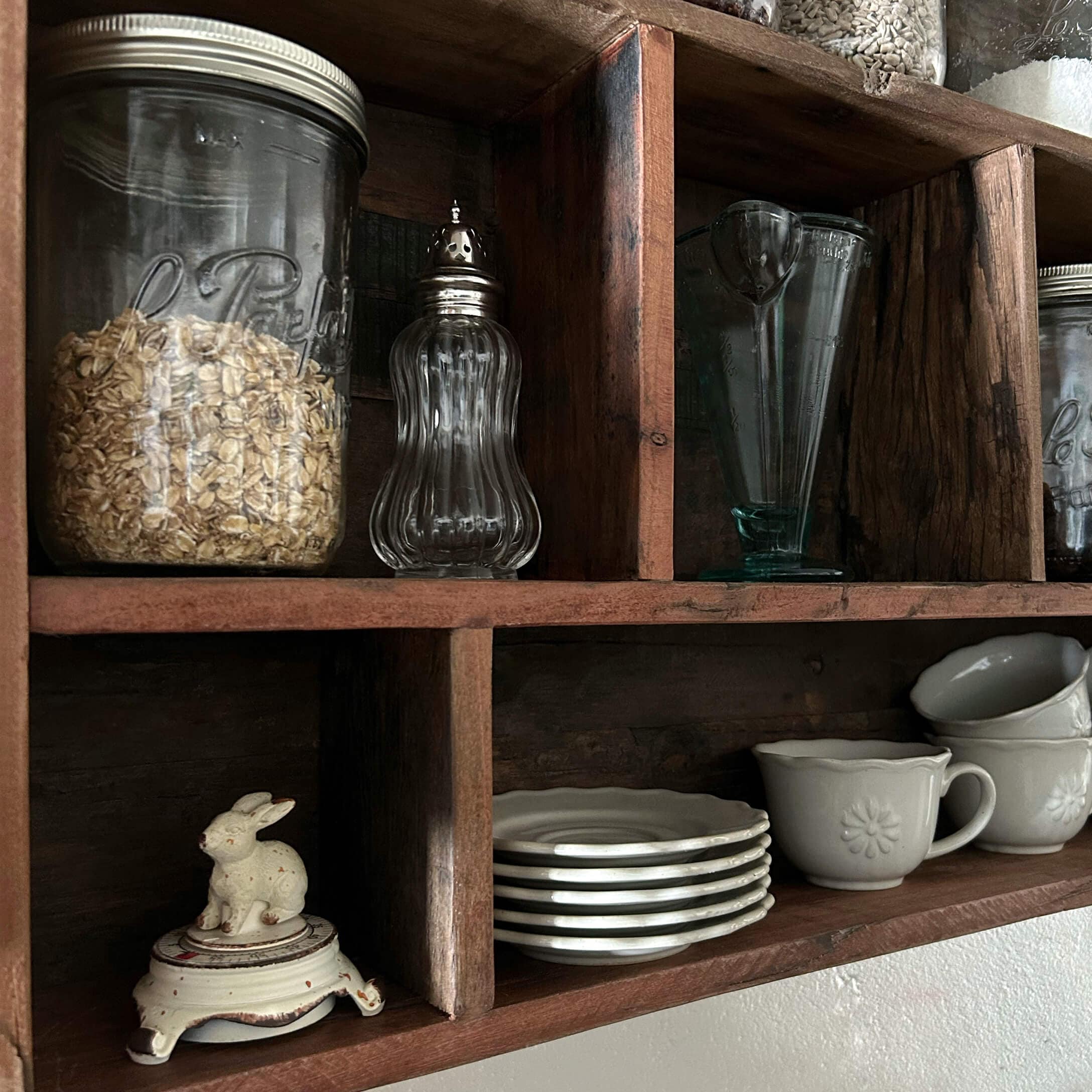 Houten plank met doorzichtige glazen potten en wit keramisch servies in keuken