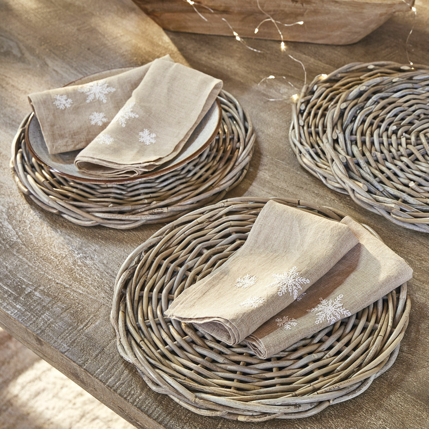 Servet set van 4 Ruspi Beige linnen servetten met sneeuwvlokborduurwerk op gevlochten rieten placemats op houten tafel