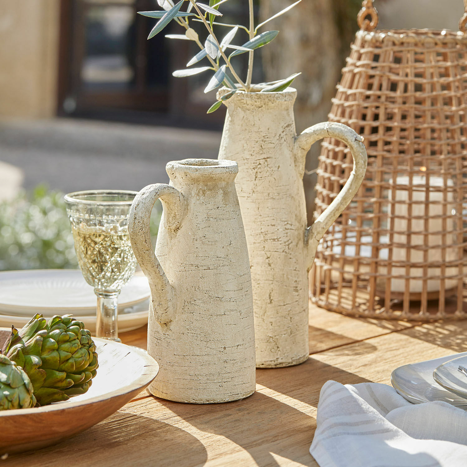 Sierkan set van 2 Lilette Twee crèmekleurige keramische kannen met handvatten op houten tafel met decoraties en glas