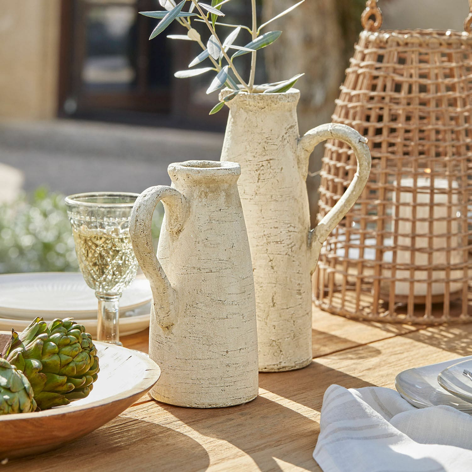 Sierkan set van 2 Lilette Twee crèmekleurige keramische kannen met handvatten op houten tafel met decoraties en glas
