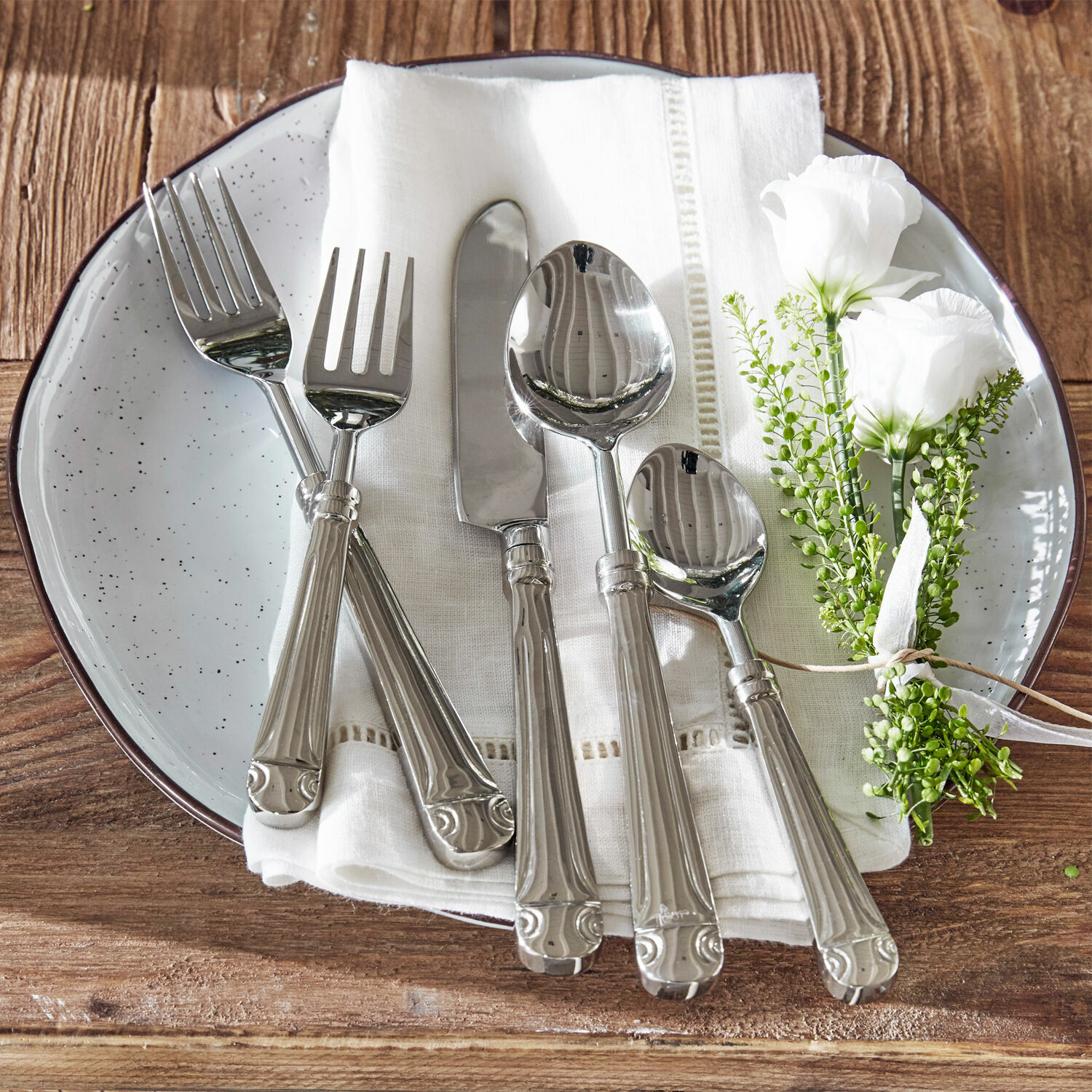 Bestek Eriat Set zilveren bestek op witte servet met bloemdecoratie op houten tafel
