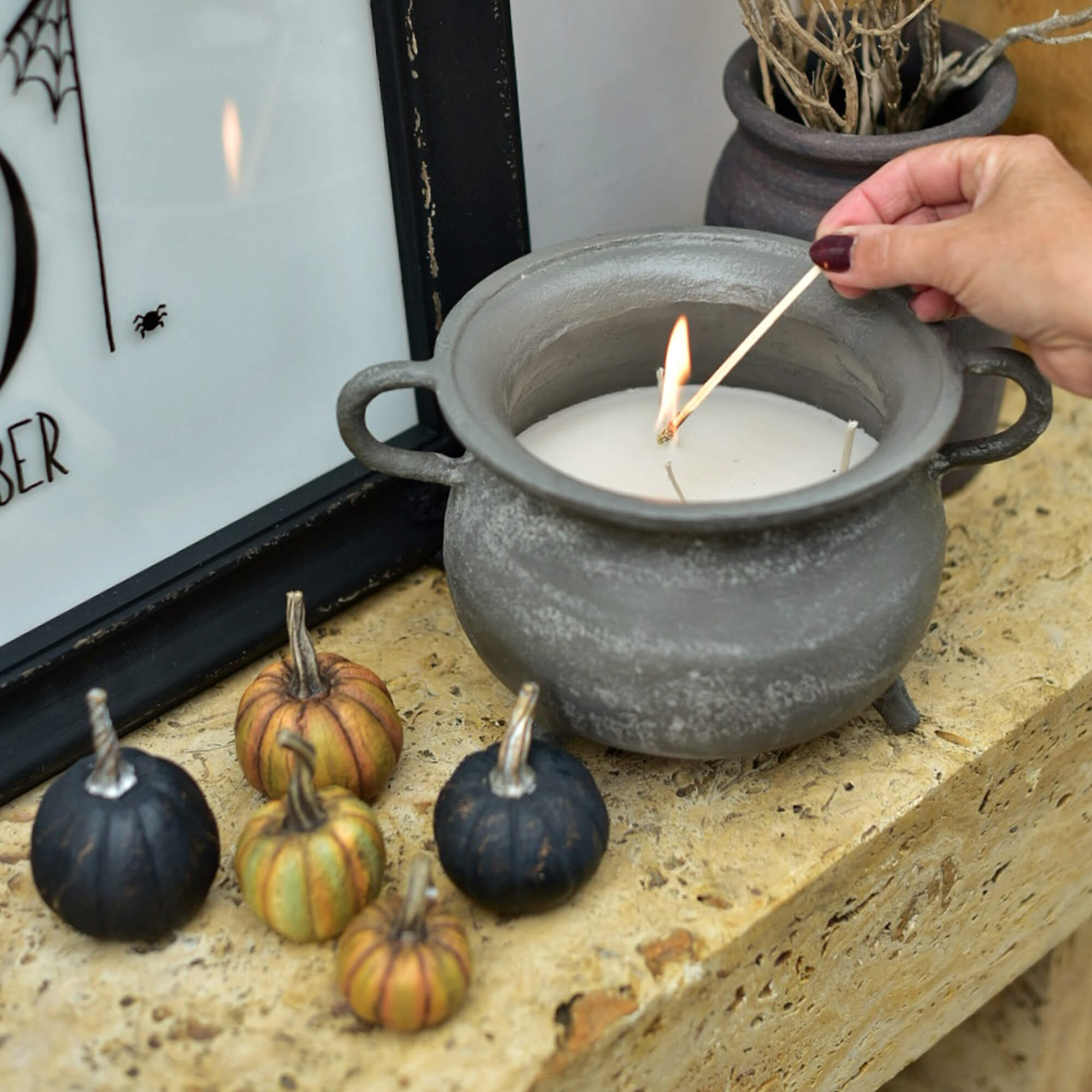 Grijze keramische kaars in ketelvorm met witte was en decoratieve mini-pompoenen op stenen vensterbank