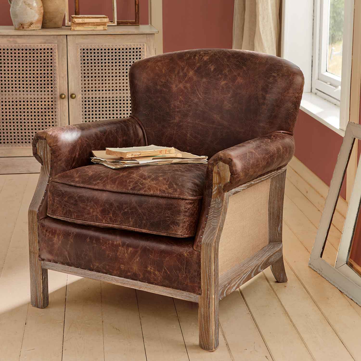 Bruine leren fauteuil met verweerde look en houten frame in rustieke kamer met boeken