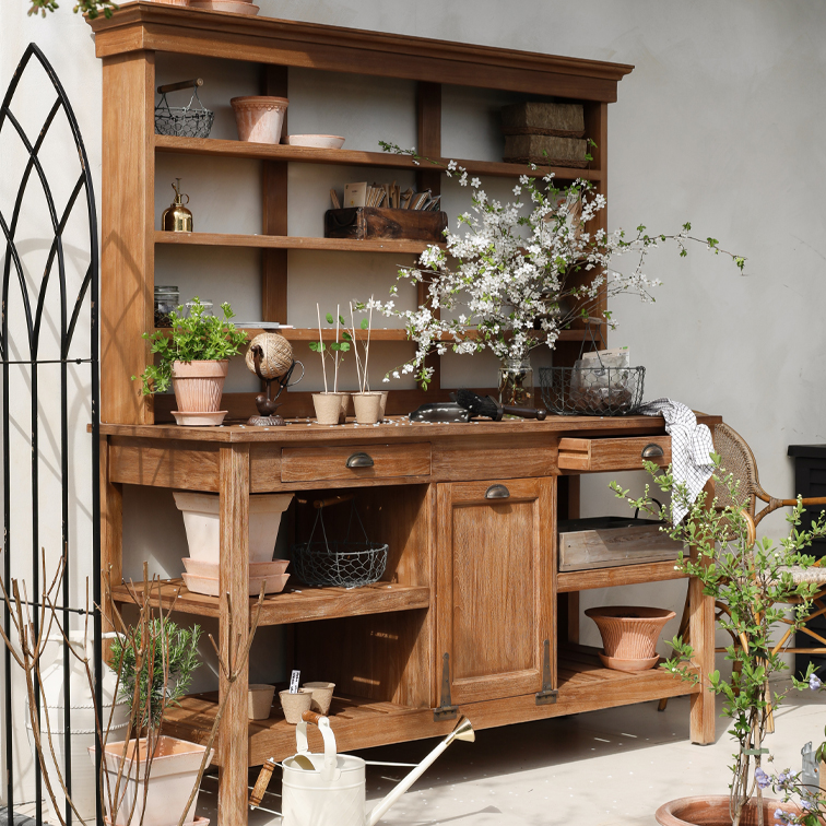 Houten tuinmeubel met planken, bloempotten en bloeiende takken, versierd met tuingereedschap