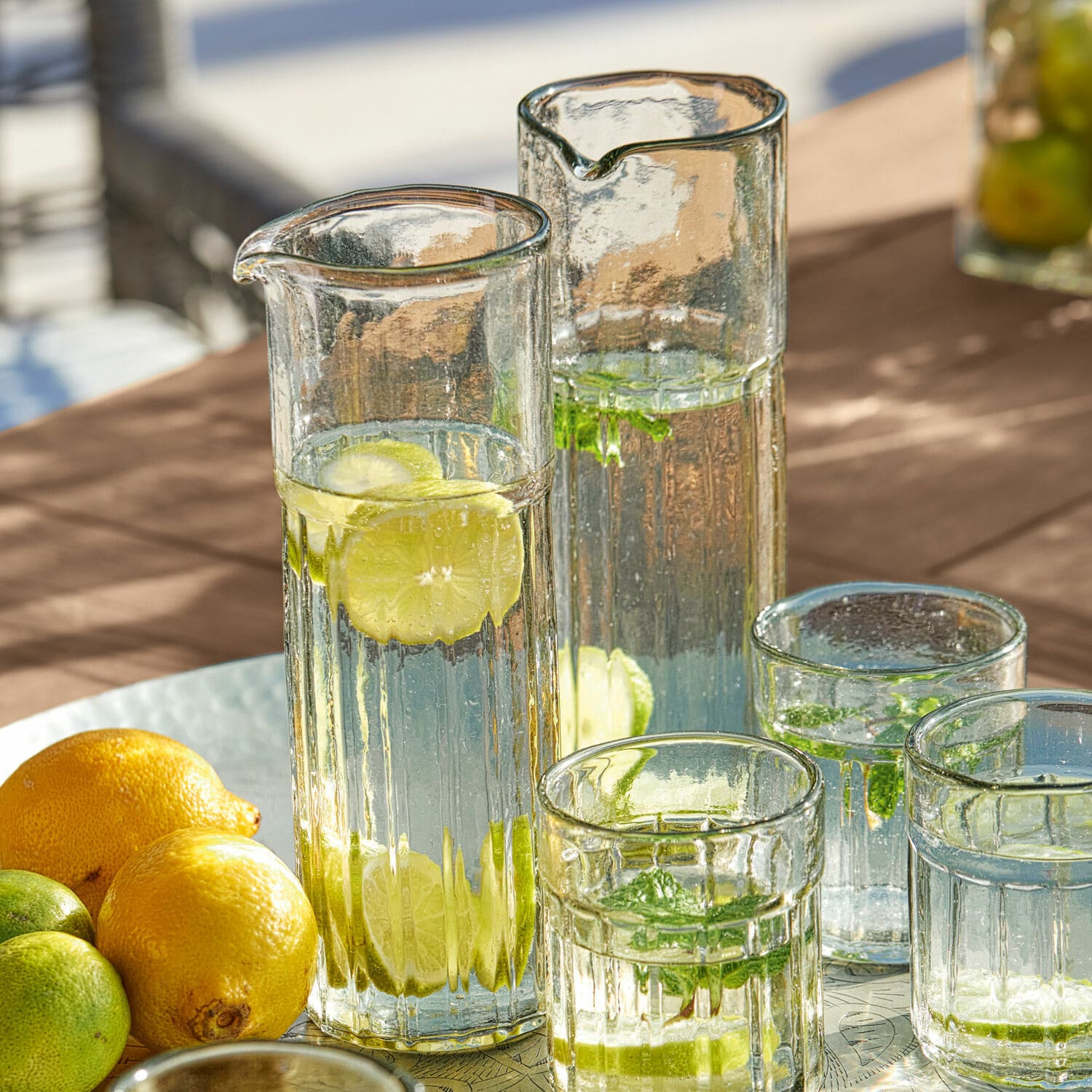 Glazen kannen en glazen met water, citroen en munt op tafel, verfrissend zomerdrankje