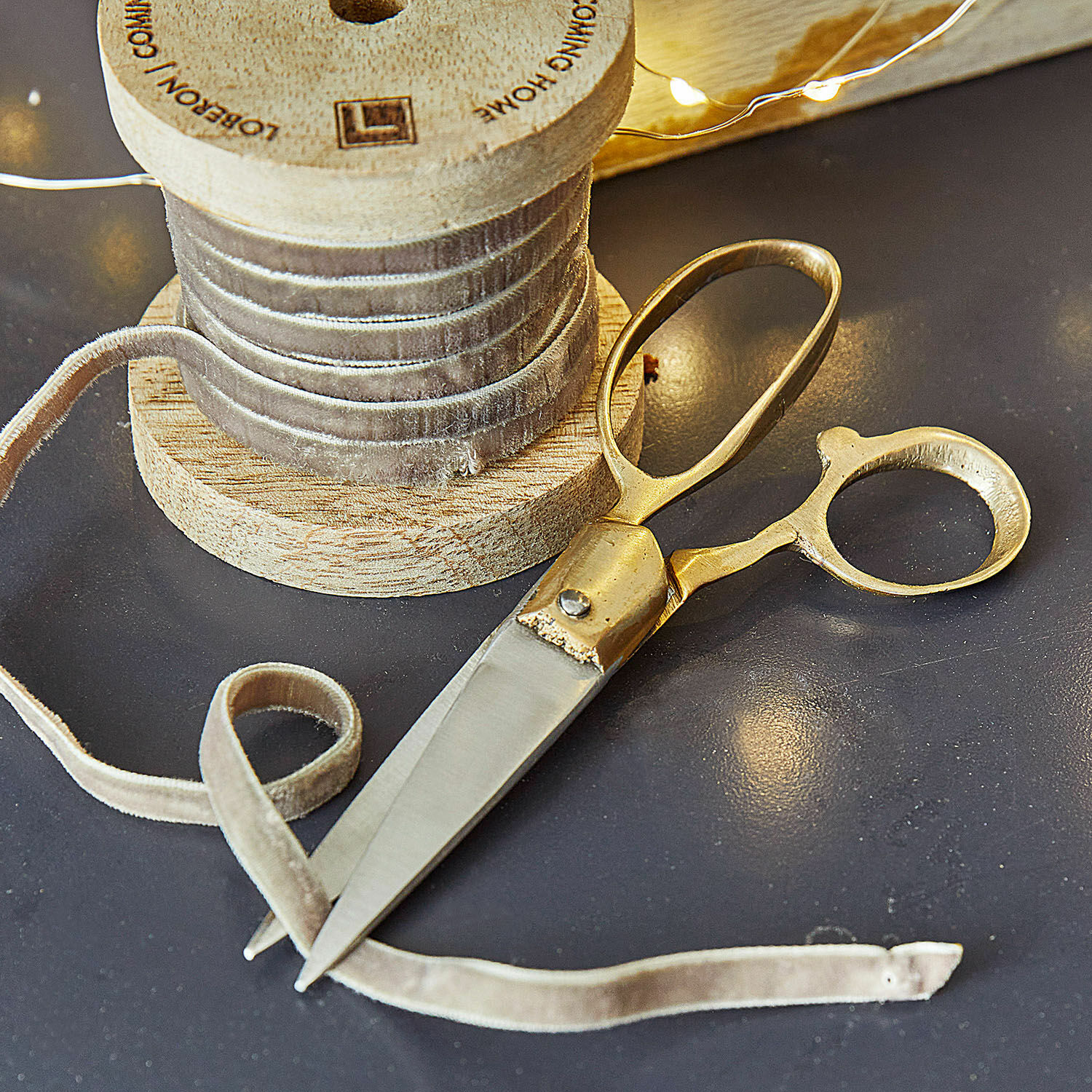 Gouden schaar en beige fluwelen lint op houten spoel op donkere tafel voor decoratie en naaien