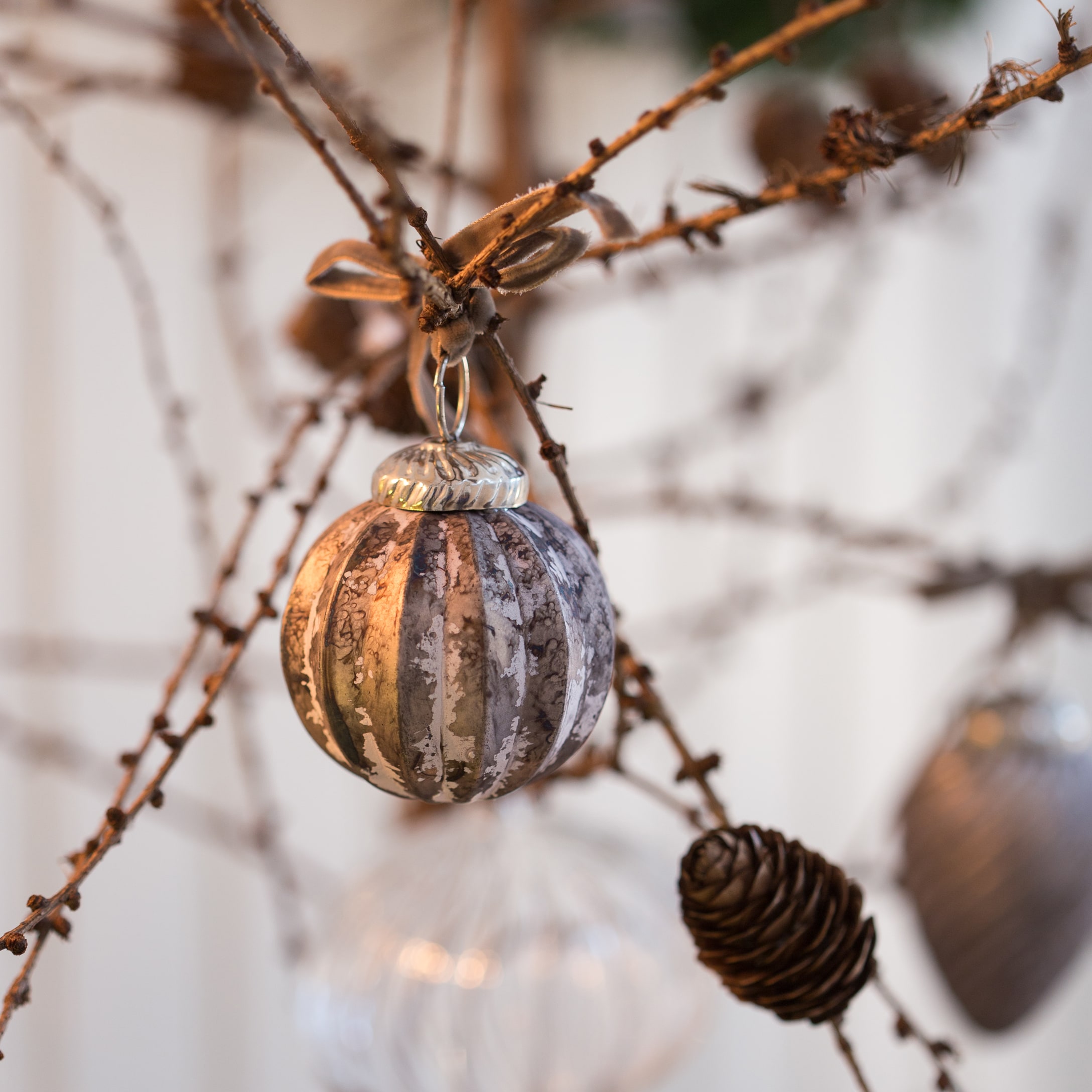 Glazen kerstbal in zilverbruine tinten aan tak met dennenappel, winterse decoratie voor thuis