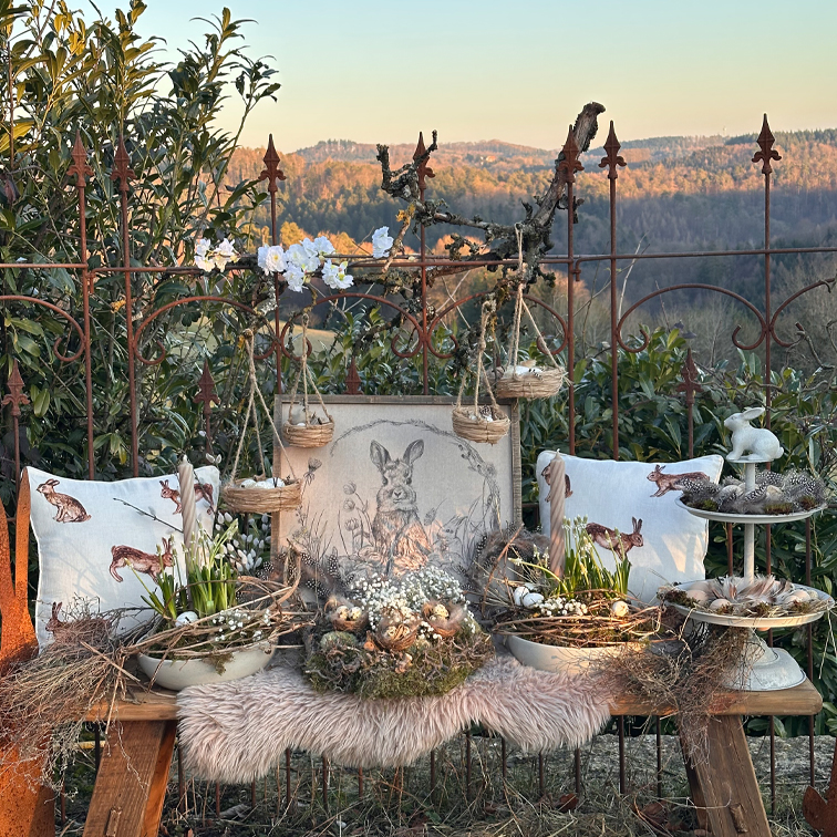 Rustieke paasdecoratie met konijnen kussens, rieten mandjes en natuurlijke bloemen op een houten bank