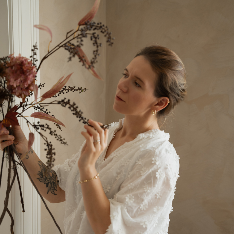 Vrouw in witte kanten blouse die droge bloemdecoratie in lichte kamer rangschikt