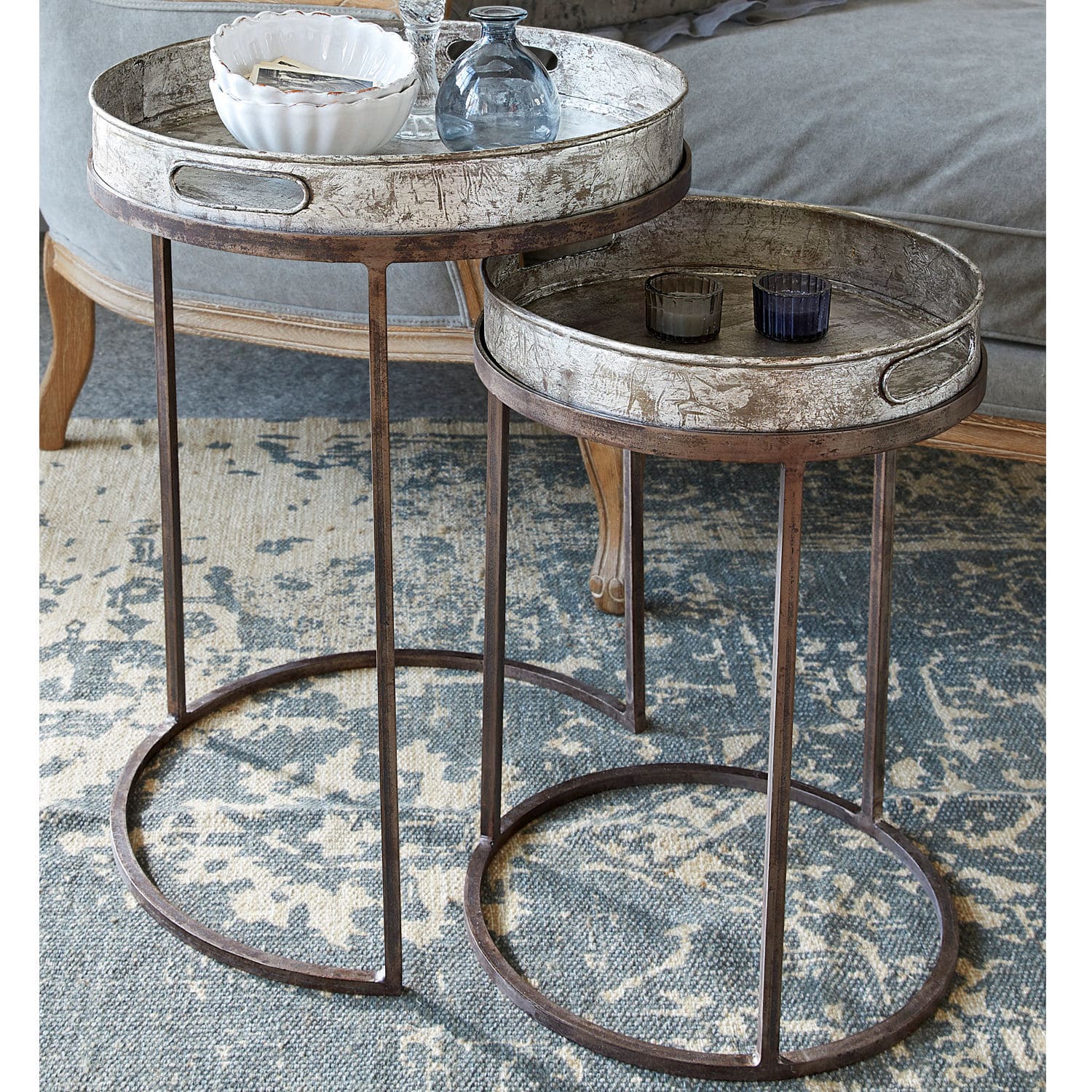 Bijzettafeltje set van 2 Saint Mark Set van twee ronde tafels met metalen frames en zilverkleurige dienbladen op een vloerkleed in de woonkamer