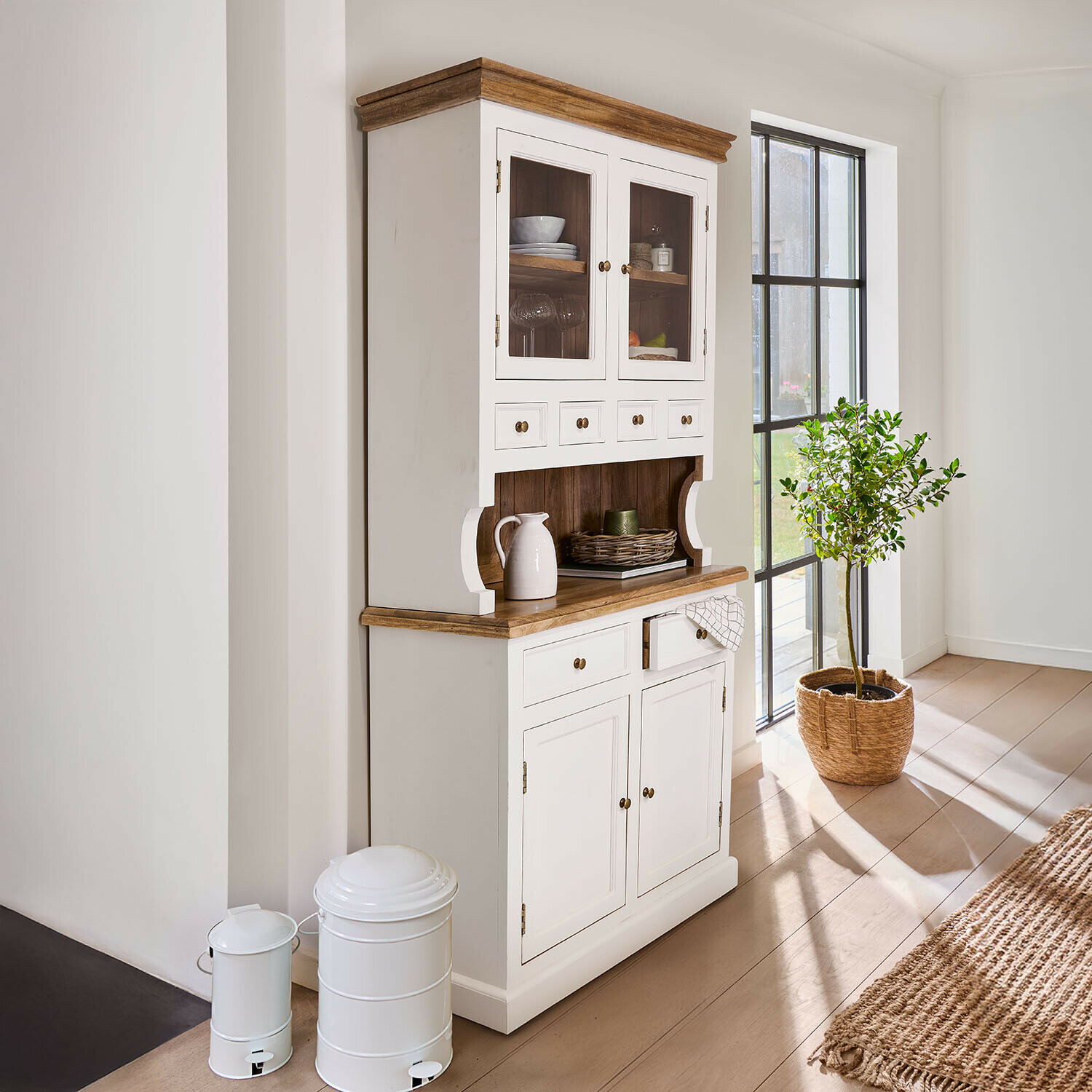 Witte houten buffetkast met natuurlijk blad en glazen deuren in lichte, zonnige kamer