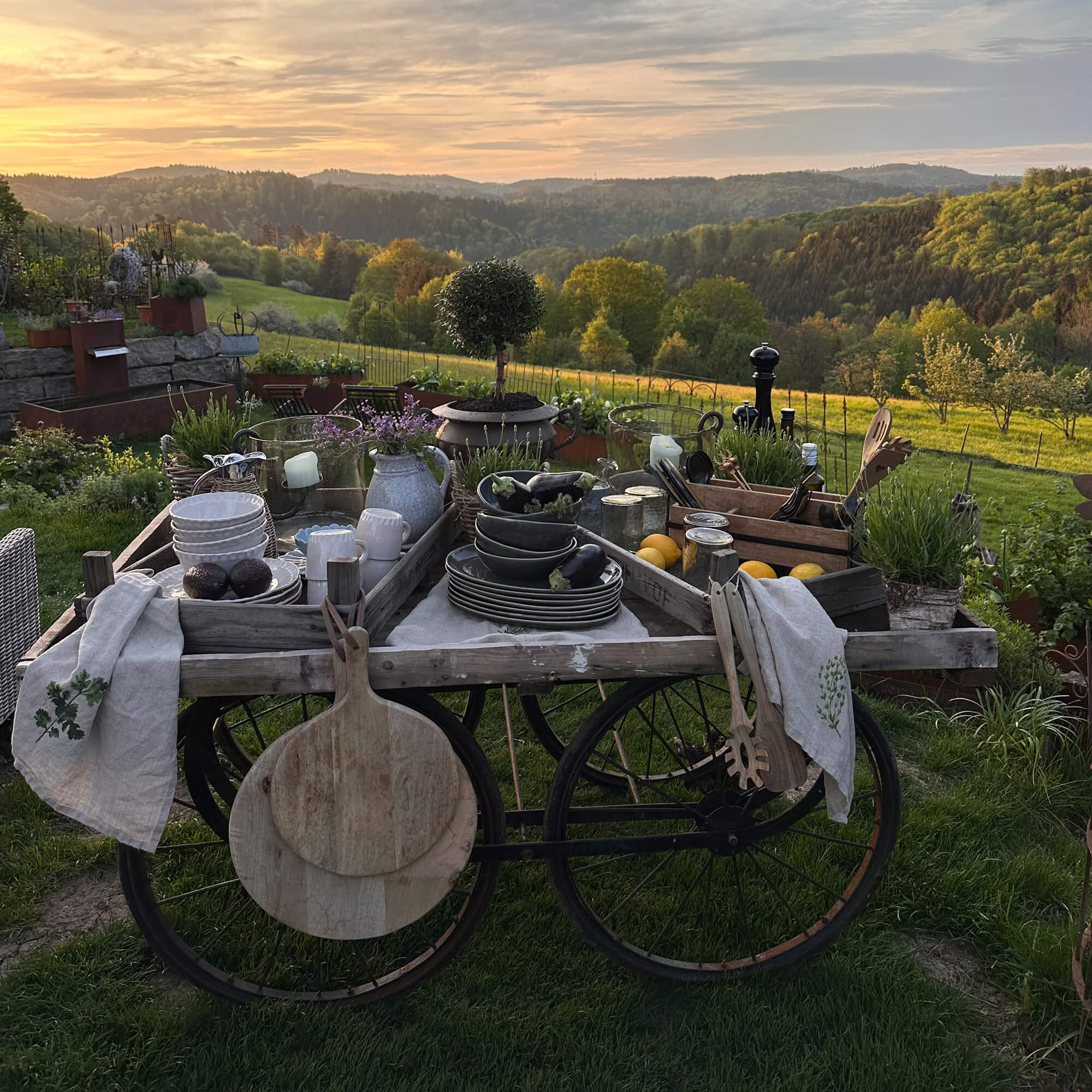 Rustieke houten kar met servies en decoraties in groene tuin bij zonsondergang