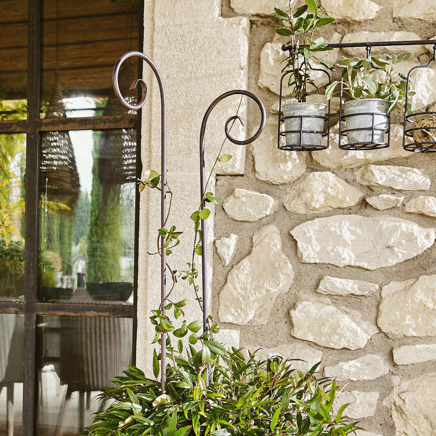 Metalen decoratieve plantensteunen in tuin bij stenen muur met groen blad