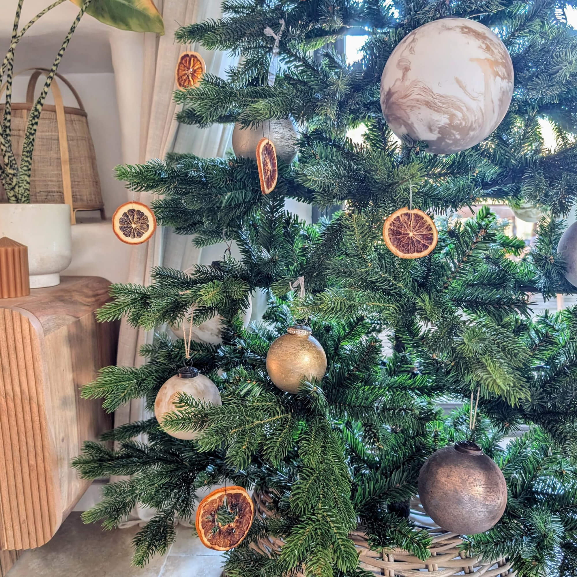 Groene kerstboom versierd met gedroogde sinaasappelschijfjes en gouden en beige kerstballen
