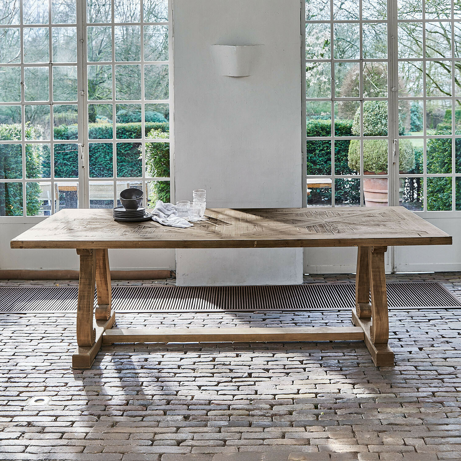 Grote eettafel van natuurlijk hout met decoratief blad voor grote ramen en een bakstenen vloer