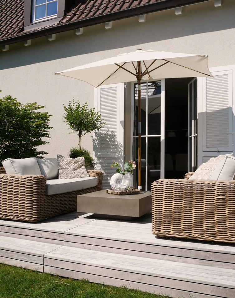 Modern beige rotan tuinmeubelset met parasol en kussens op licht houten terras