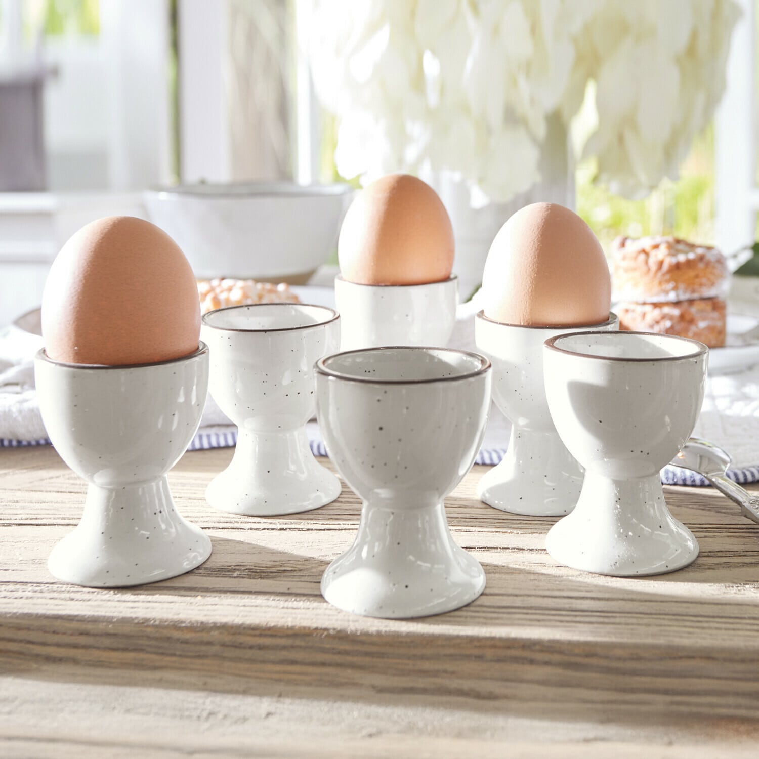 Eierdopje set van 6 Biarré Set witte keramische eierdopjes met bruine eieren op een lichte houten tafel